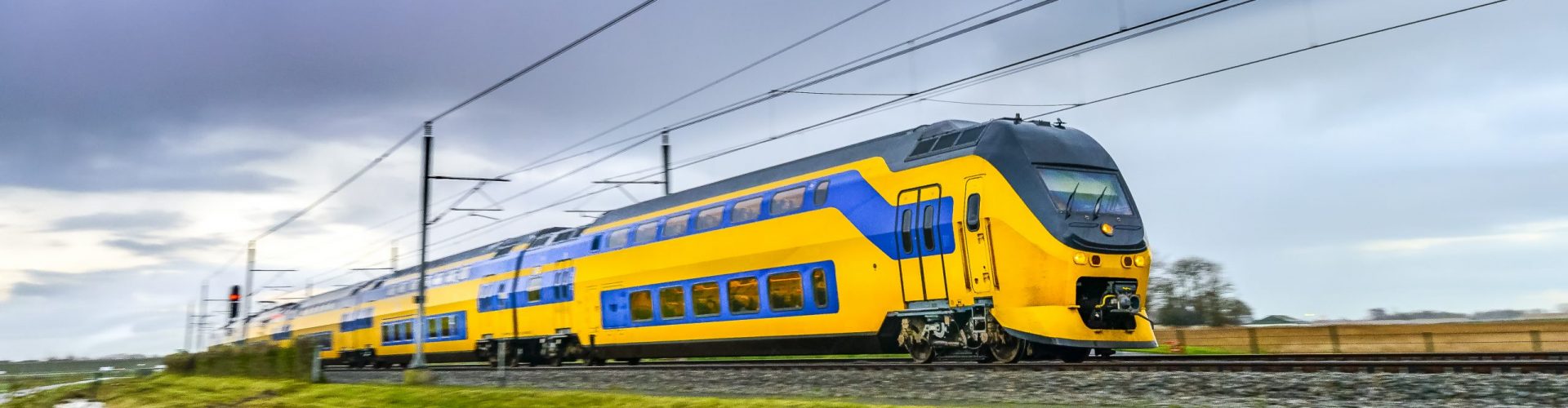 Yellow and blue Dutch passenger train driving through a rural landscape on a dark and rainy fall day. Image with speed effect from the motion blur.
